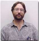 Headshot of Zauhar. He is wearing large glasses and a patterned shirt. He has a short beard. 