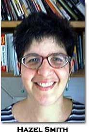 Hazel Smith with short hair and glasses smiles for the camera wearing a striped shirt